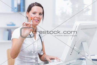 Doctor holding an injection in front of computer at clinic