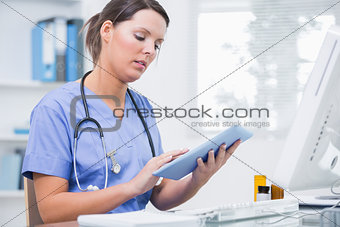 Female surgeon using digital tablet in front of computer at clinic
