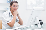 Nurse with hands under chin in front of computer at clinic
