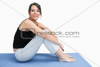 Side view of young woman in sportswear sitting on yoga mat