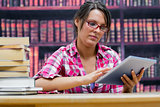 College student using digital tablet with stack of books at library