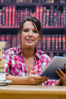 College student with digital tablet and stack of books at library