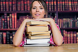 Portrait of college student sitting with stack of books in library