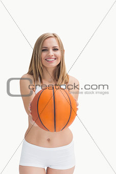 Happy woman in sportswear holding out basketball