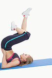 Side view of woman in shoulder stand cycle position on yoga mat