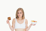 Woman with fruit bowl making faces as she looks at cookie