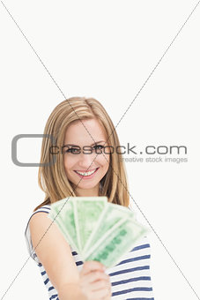 Portrait of happy young woman holding out fanned dollar banknotes