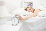 Irritated woman in bed extending hand to alarm clock