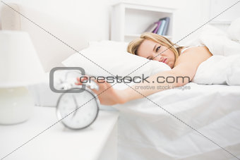 Irritated woman in bed extending hand to alarm clock