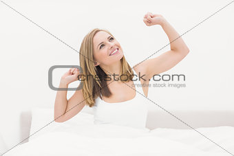 Smiling woman waking up in bed and stretching her arms up