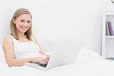 Portrait of happy woman using laptop in bed
