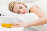 Asleep woman with focus on spilt bottle of pills at home