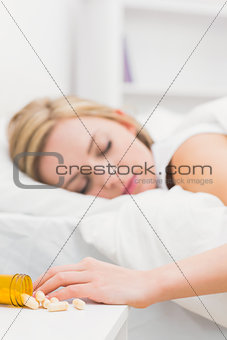 Asleep woman with focus on spilt bottle of pills at home