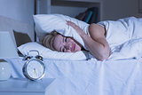 Woman covering ears with pillow as alarm clock rings