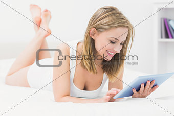 Beautiful happy woman lying in bed and using digital tablet