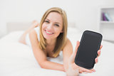 Portrait of woman showing smartphone in bed
