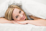 Portrait of beautiful woman under sheet in bed