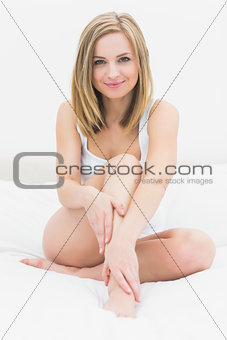 Woman applying cream on leg while sitting on bed