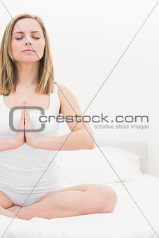 Woman in praying position with eyes closed on bed