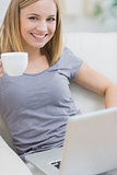Smiling woman with coffee cup using laptop on sofa