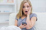 Portrait of casual shocked woman with cellphone at home