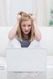 Frustrated casual woman with head in hands in front of laptop at home