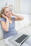 Happy woman listening music through headphones with laptop