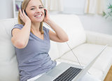 Happy woman listening music through headphones with laptop