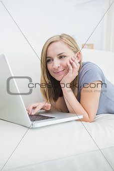 Casual woman lying on couch and using laptop