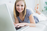 Portrait of casual woman lying on couch and using laptop