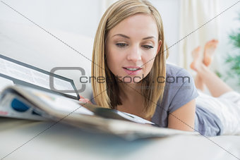 Casual woman reading magazine while lying on couch