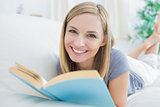 Portrait of happy woman with storybook lying on couch
