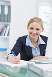 Smiling business woman writing notes at office desk