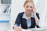 Business woman writing while on call at desk in office