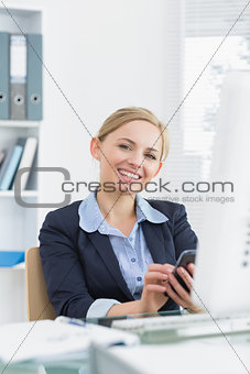 Portrait of smiling business woman with cellphone at office desk