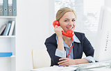 Smiling female executive using red land line phone at desk