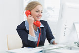 Female executive using red land line phone at desk