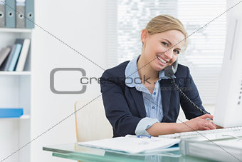 Portrait of business woman using phone and computer at desk