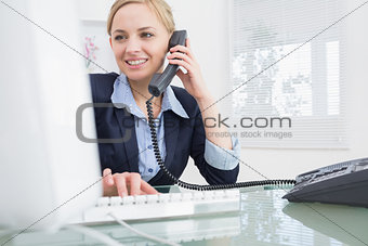Female executive using phone and computer at office