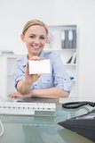 Happy female executive holding out blank card at office