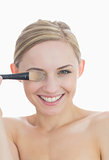 Closeup of playful woman covering eye with makeup brush