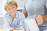 Smiling boy having cereal with father pouring milk