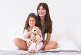 Mother and daughter sitting on bed with teddy bear