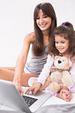 Mother and daughter using laptop with teddy bear