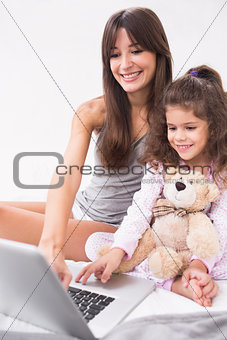 Mother and daughter using laptop with teddy bear