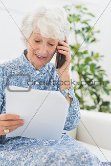 Elderly happy woman reading a paper on the phone