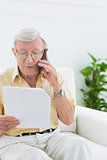 Elderly focused man reading papers on the phone