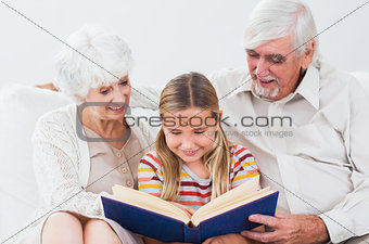 Granddaughter reading book with grandparents