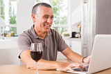 Happy man using laptop with glass of red wine