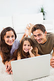 Smiling family lying on a carpet with the laptop